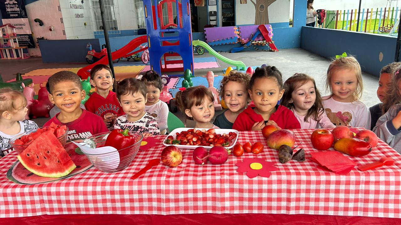 Crianças olhando para a mesa cheia de frutas e legumes da cor vermelha