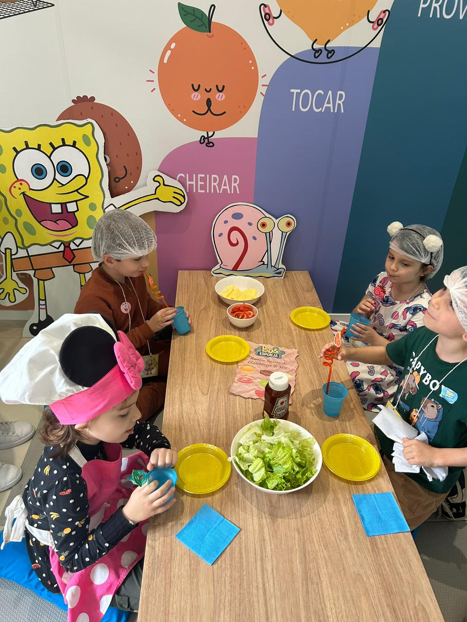 Crianças à mesa esperando o hambúrguer ficar pronto